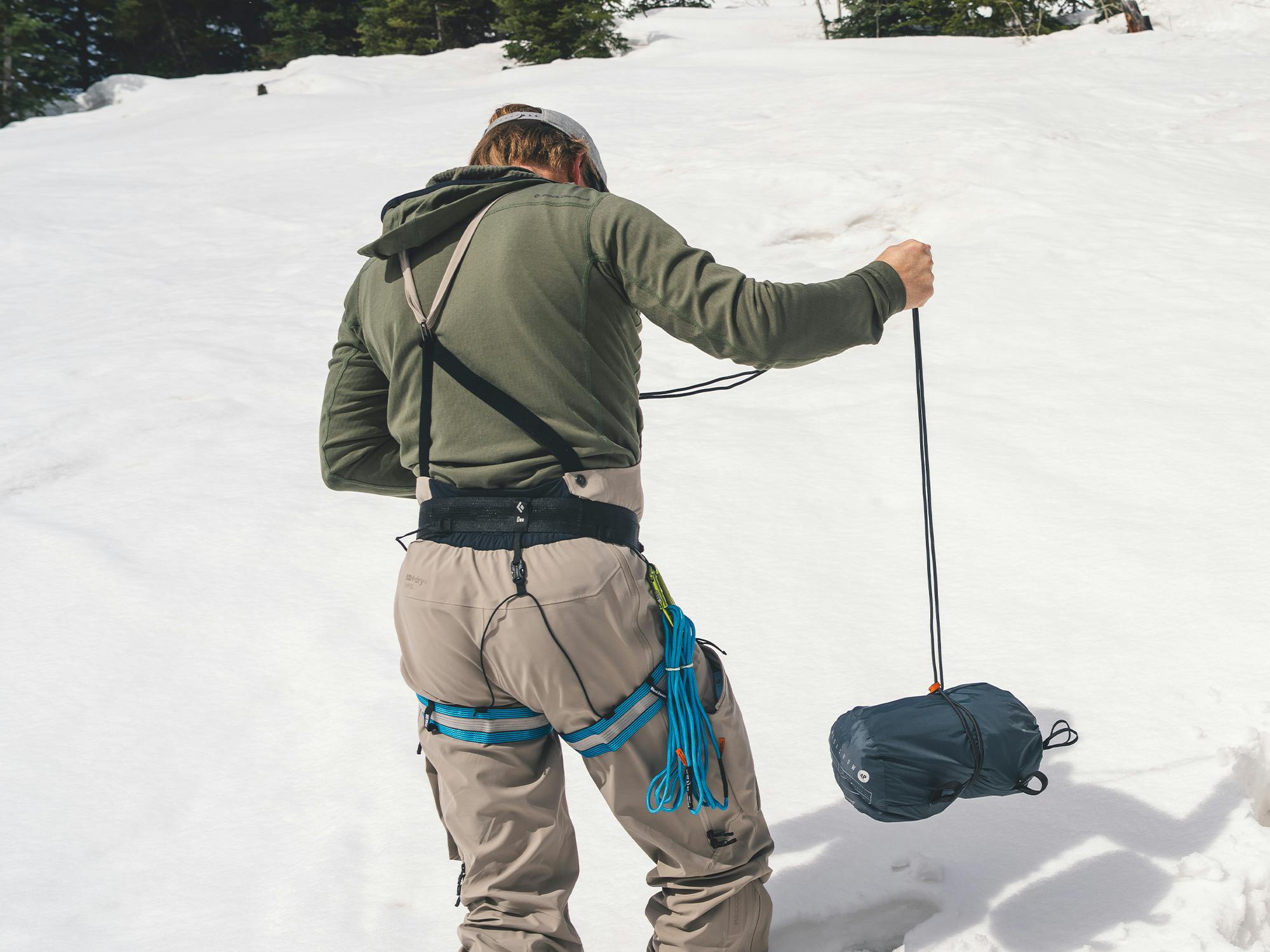 A man builds a snow anchor with a stuff sack